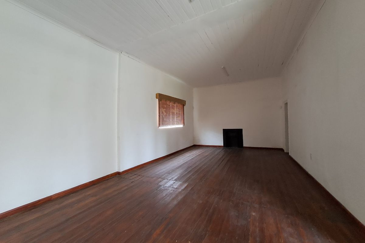 A spacious, empty living room featuring original timber flooring, a built-in fireplace, and a high timber-paneled ceiling.