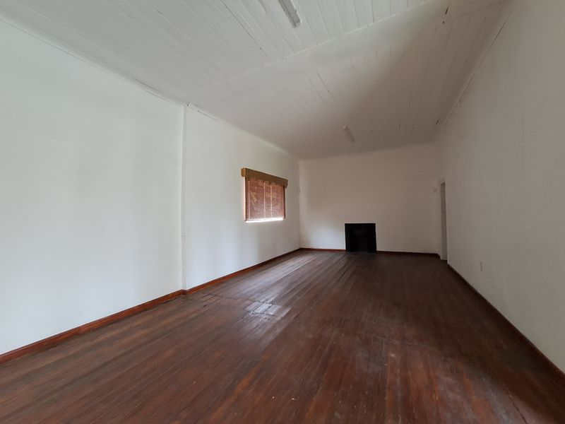 A spacious, empty living room featuring original timber flooring, a built-in fireplace, and a high timber-paneled ceiling.