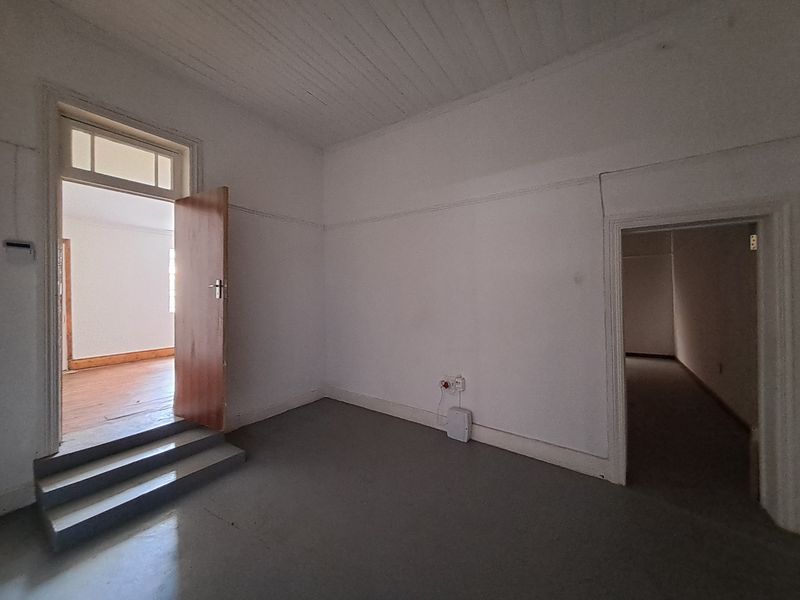 An empty, neutrally painted room featuring high ceilings, timber door frames, and a step-down transition to an adjacent living area.