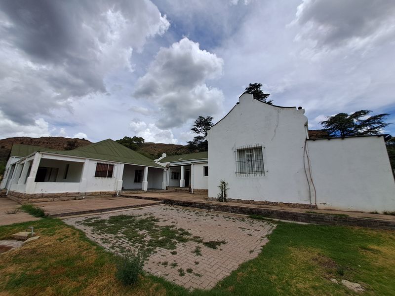 A view of the rear exterior of the house featuring a paved courtyard, covered patio areas, and traditional white-walled architecture with green roofing.