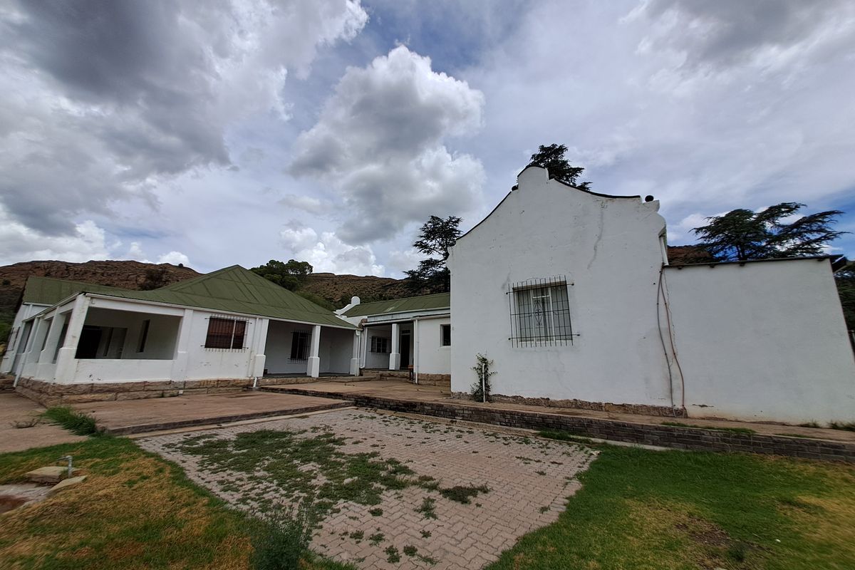 A view of the rear exterior of the house featuring a paved courtyard, covered patio areas, and traditional white-walled architecture with green roofing.