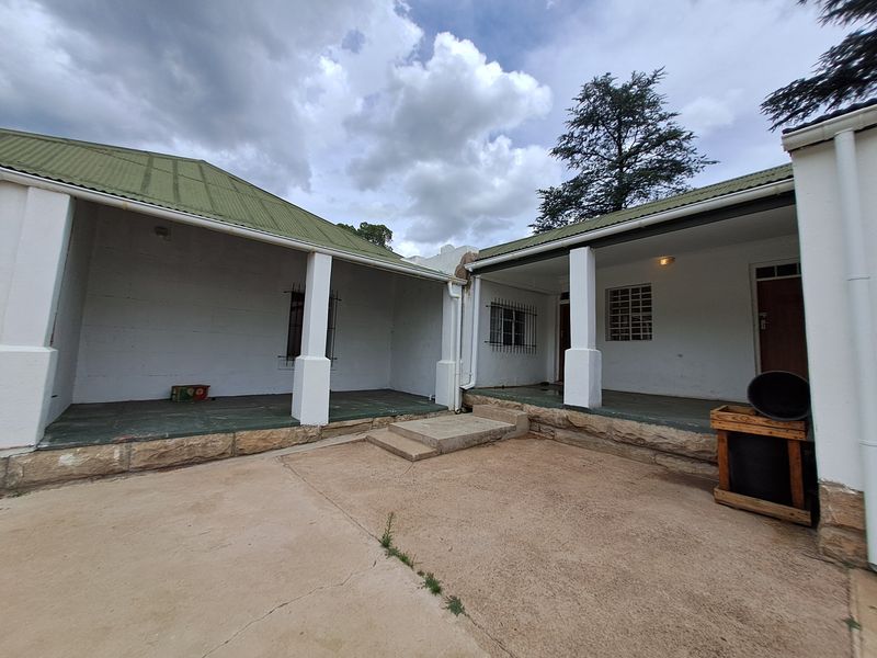 A rear exterior view of the house featuring a covered patio area, concrete courtyard, and traditional pitched roof structure.