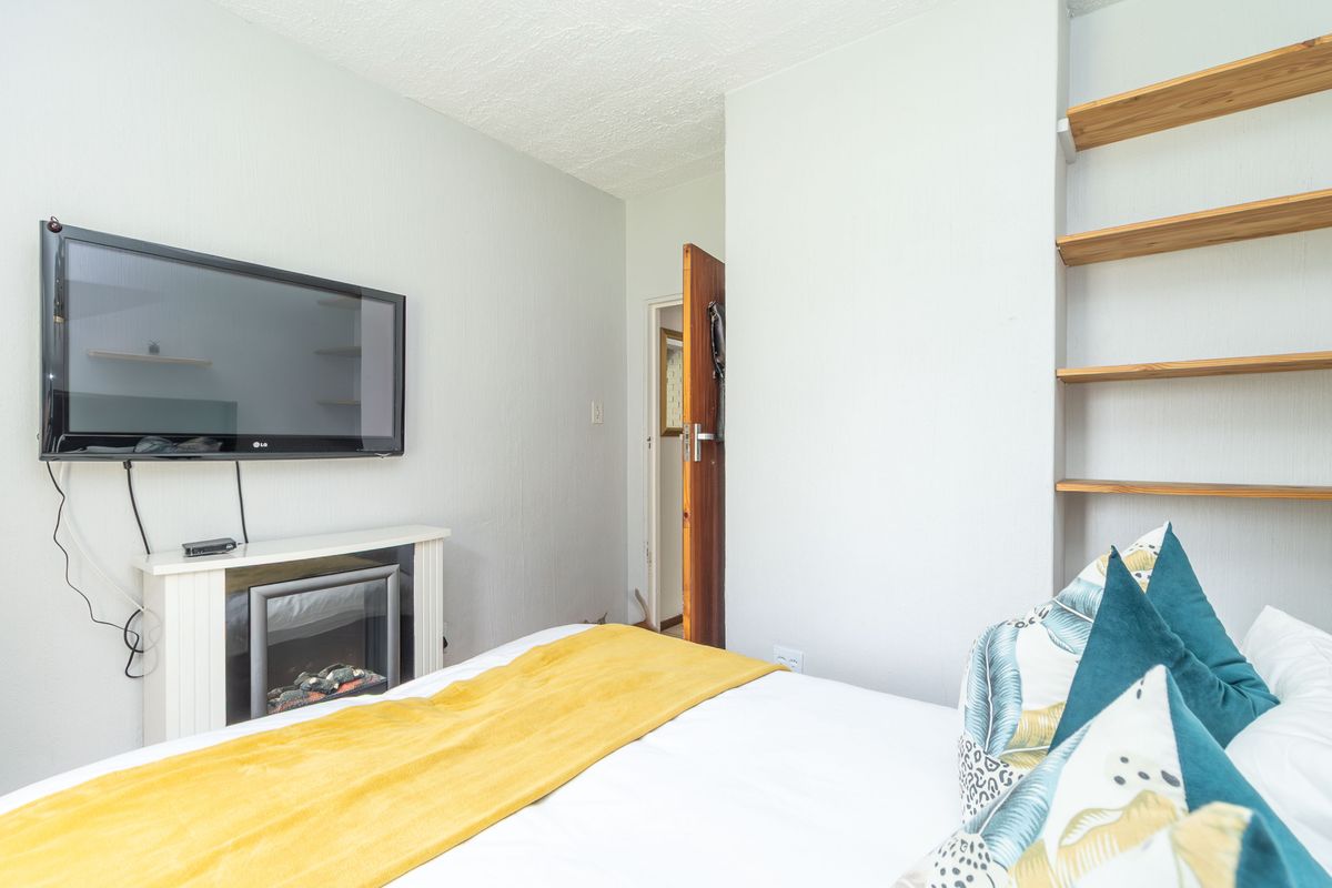 A bedroom featuring built-in timber shelving and a wall-mounted electric fireplace, providing a cozy and functional living space.