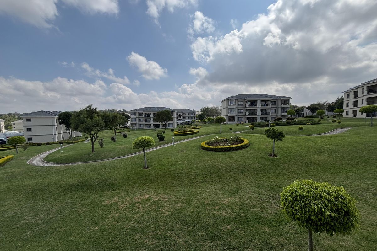 A wide-angle view of a well-maintained apartment complex featuring expansive green lawns, manicured garden beds, and paved pathways between residential buildings.