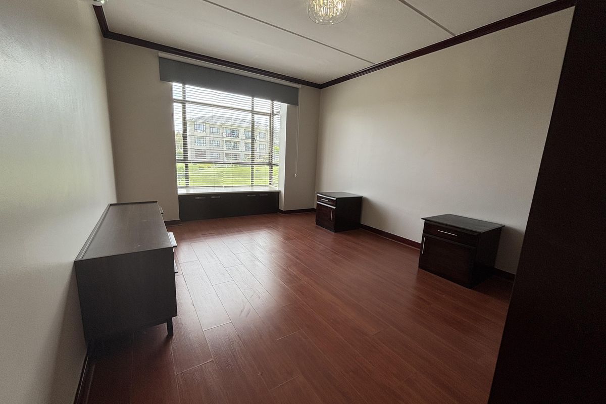 A spacious bedroom featuring laminate flooring, a built-in window seat with storage, and an air conditioning unit, offering a clean and neutral living space.