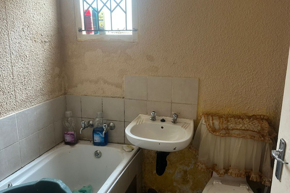 A dated bathroom featuring a standard bathtub, wall-mounted basin, and toilet, requiring significant cosmetic renovation and repair to wall finishes.