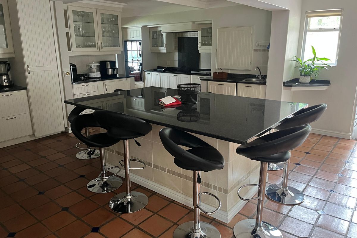 Spacious kitchen featuring a large central island with granite countertops, ample cabinetry, and terracotta tile flooring.