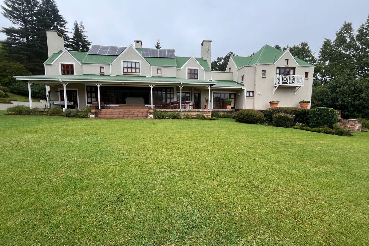 Spacious rear elevation of a large residence featuring a covered patio, green metal roof, solar panels, and expansive manicured lawn.