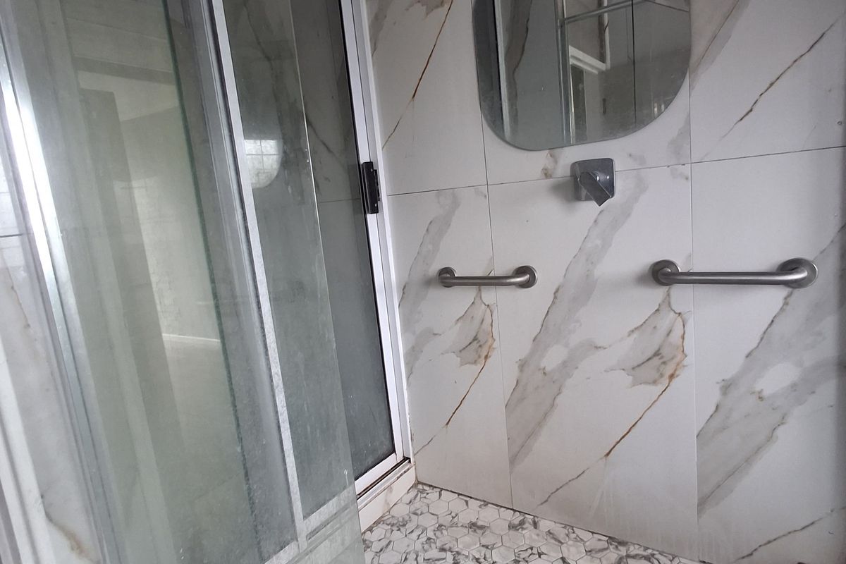 Modern bathroom featuring a walk-in shower with glass enclosure, rainfall shower head, marble-look wall tiles, and hexagonal floor tiling with safety grab rails.