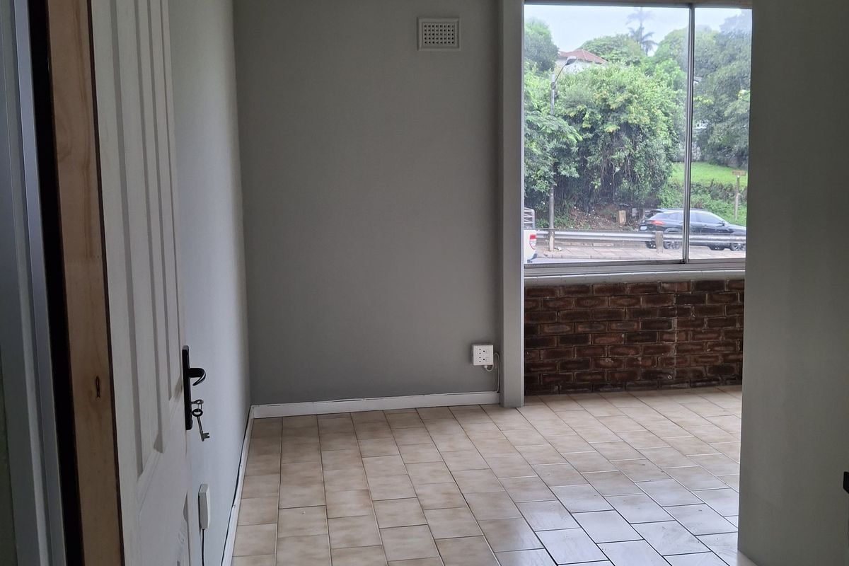 An empty bedroom featuring tiled flooring, a large window with a view, and exposed brick detailing. The room requires minor finishing touches.