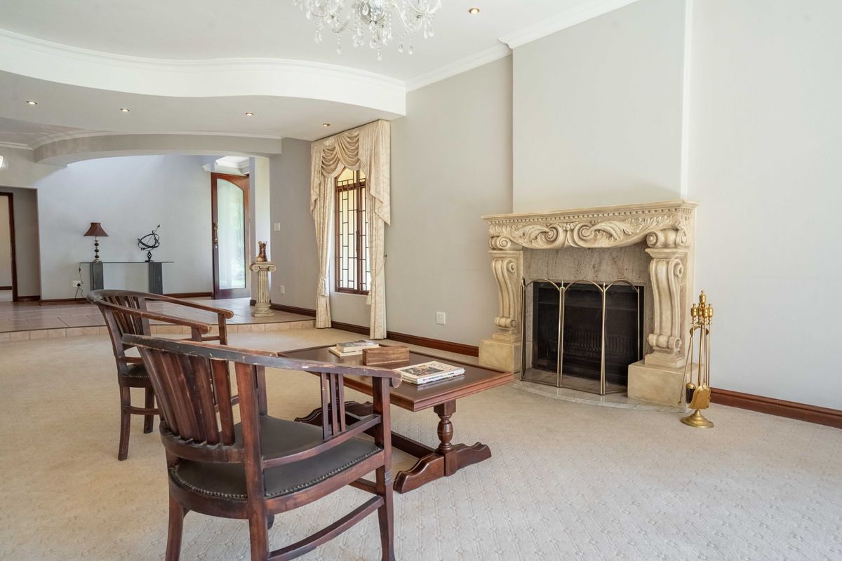 Spacious living room featuring an ornate stone fireplace, coved ceilings with recessed lighting, and a chandelier, leading into a tiled entryway.