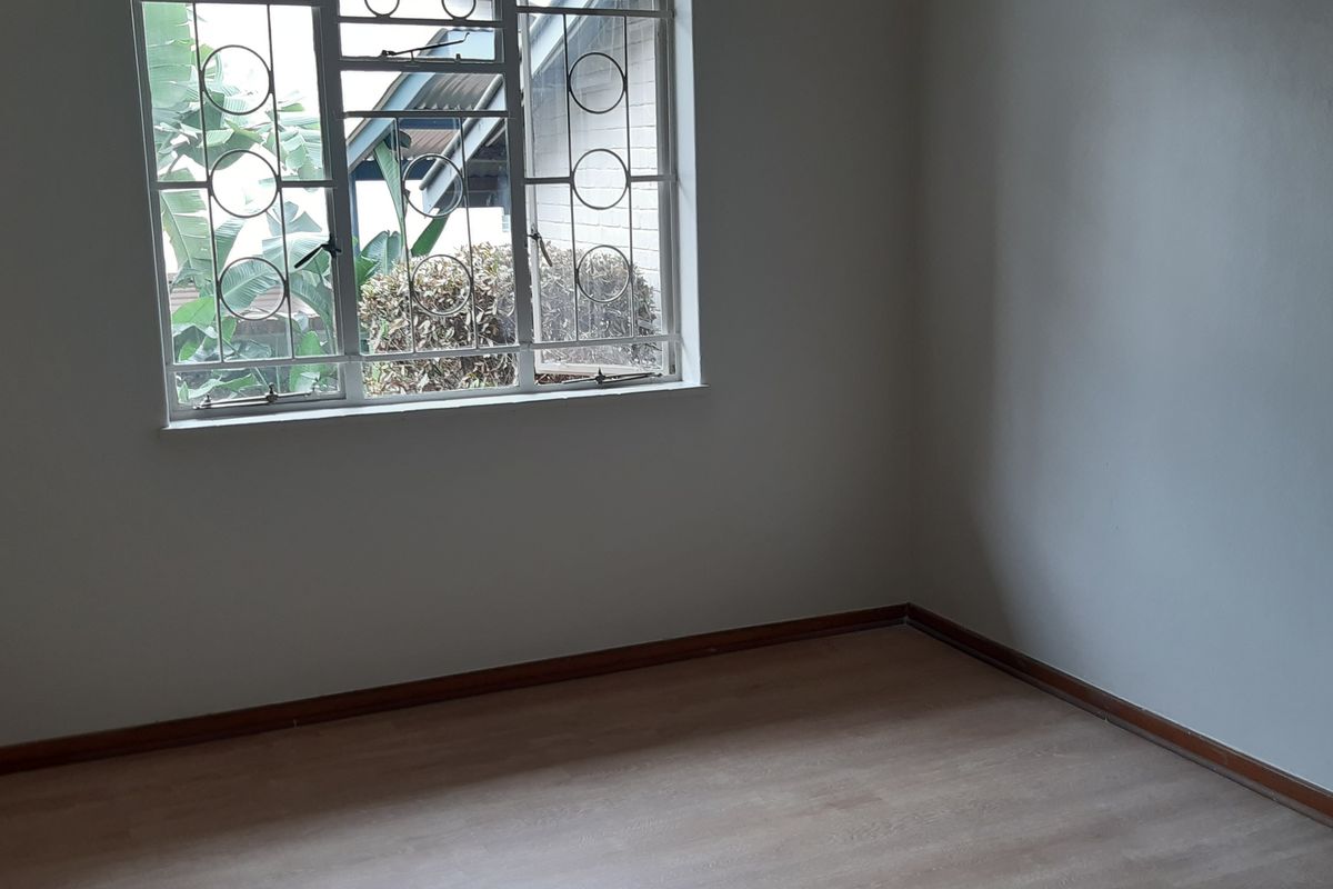 A clean, empty bedroom featuring light-toned laminate flooring, neutral walls, and a window fitted with security bars.