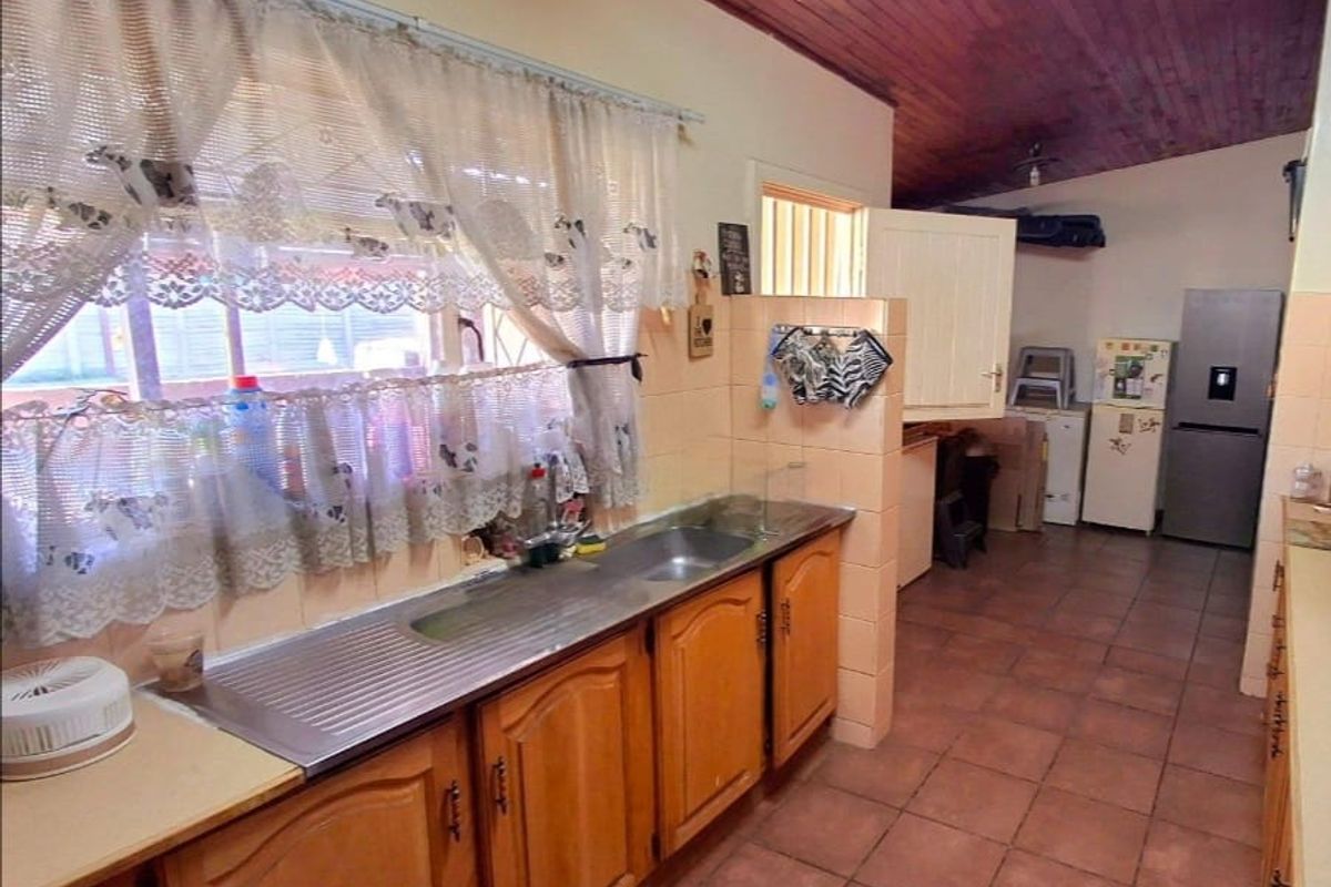 A functional kitchen featuring wooden cabinetry, a stainless steel sink, tiled flooring, and a timber-paneled ceiling, offering a traditional layout with ample storage space.