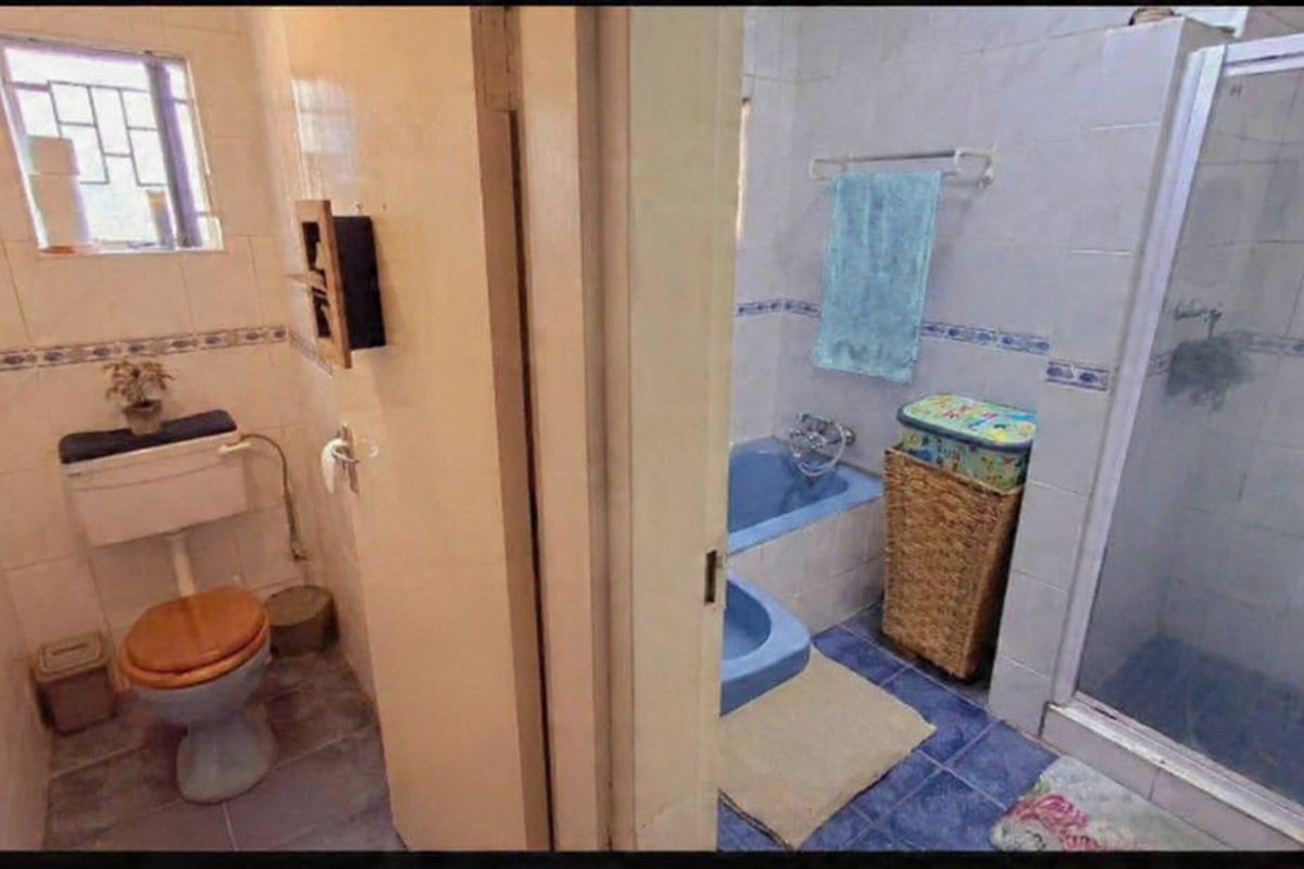 A split-view bathroom featuring a separate toilet area and a combined shower and bathtub area with dated blue sanitary ware and wall tiling.