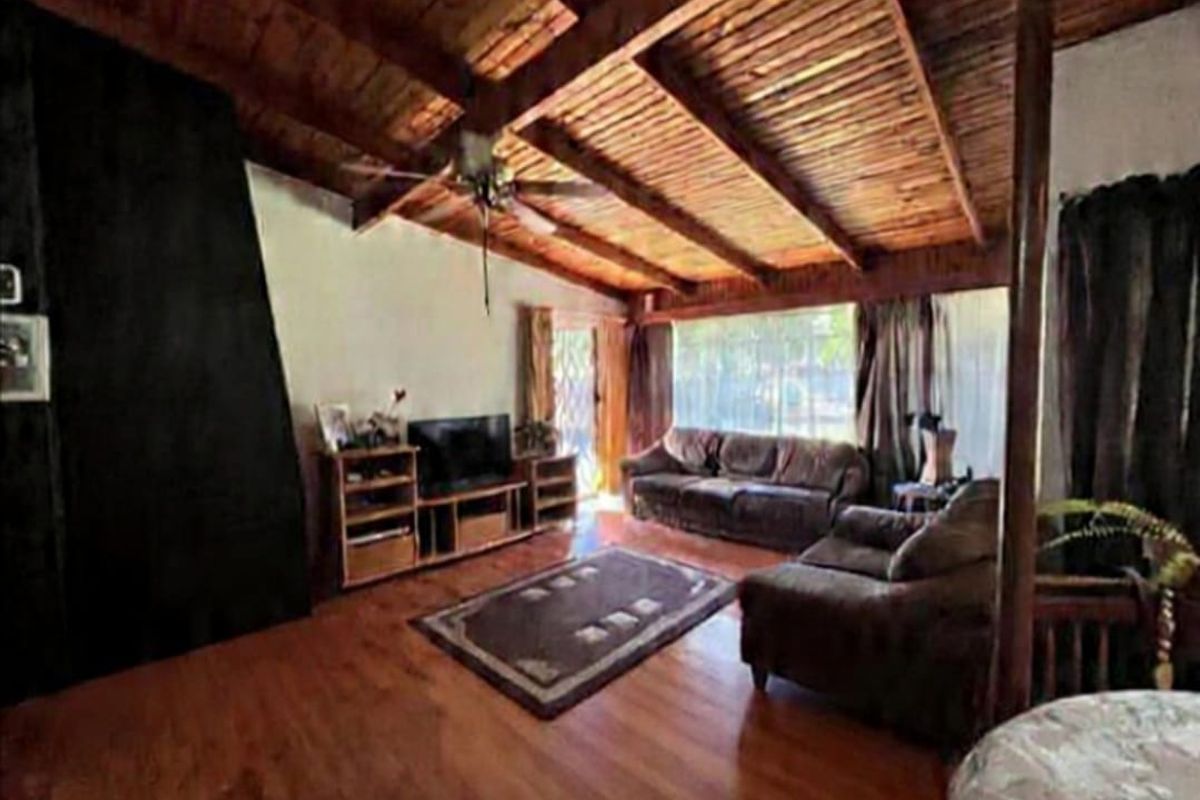 Spacious living room featuring exposed timber beam vaulted ceilings, wood-look flooring, and a prominent dark feature wall.