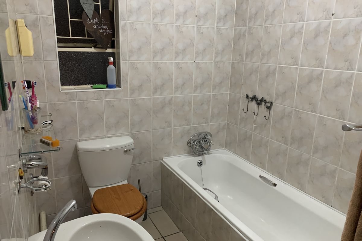 A functional bathroom featuring a standard bathtub, toilet, and pedestal basin with neutral wall tiling and security bars on the window.