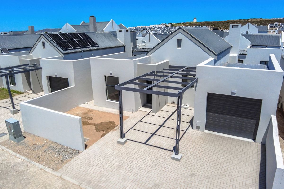 Aerial view of a modern residential property featuring a paved driveway, garage, pergola, and solar panels on a pitched metal roof.