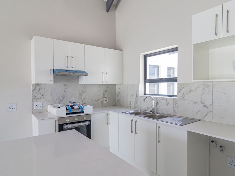 Modern kitchen featuring white cabinetry, quartz countertops, marble-look splashback, built-in oven, extractor fan, and a stainless steel sink.
