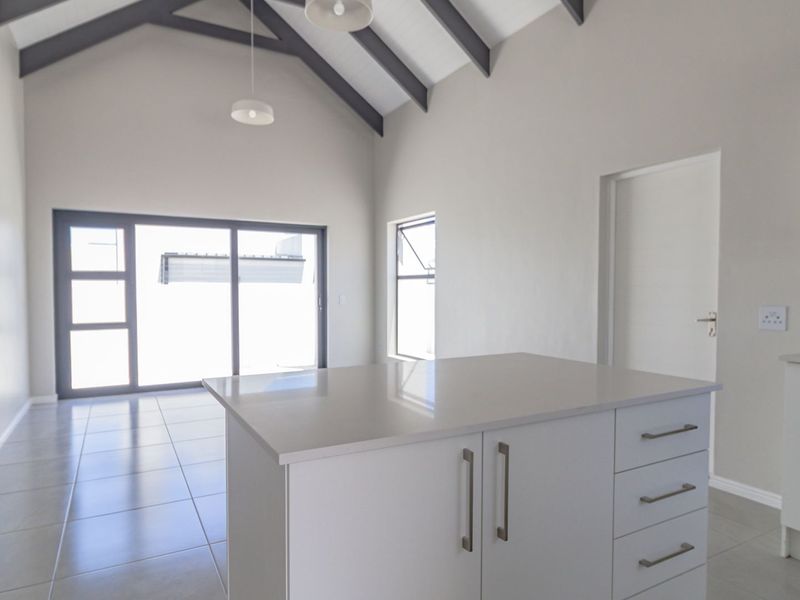 Modern open-plan living area featuring a kitchen island, built-in oven, vaulted ceilings with exposed rafters, and large sliding glass doors leading outdoors.