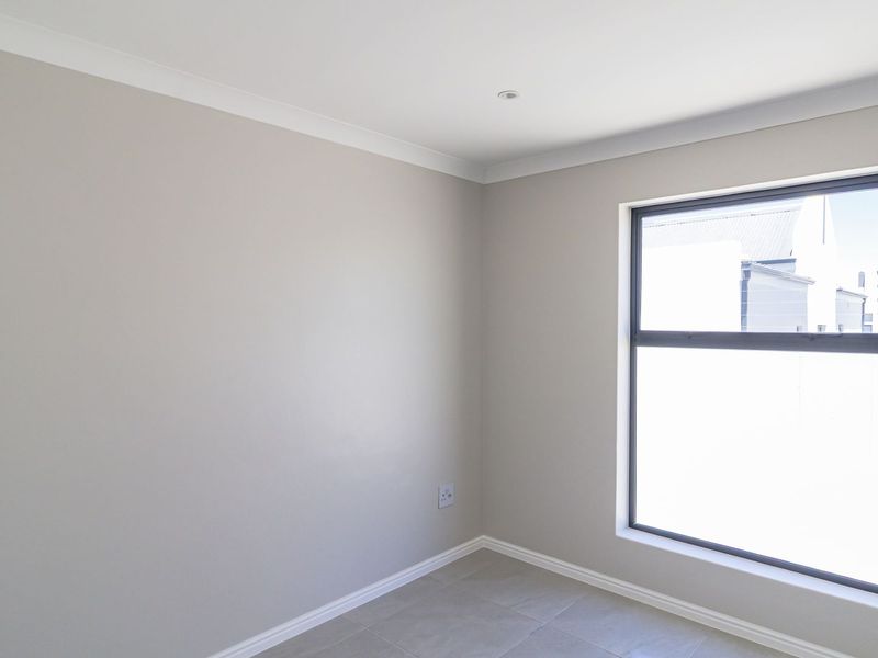A bright, empty bedroom featuring neutral wall tones, tiled flooring, and a large aluminium-framed window providing natural light.