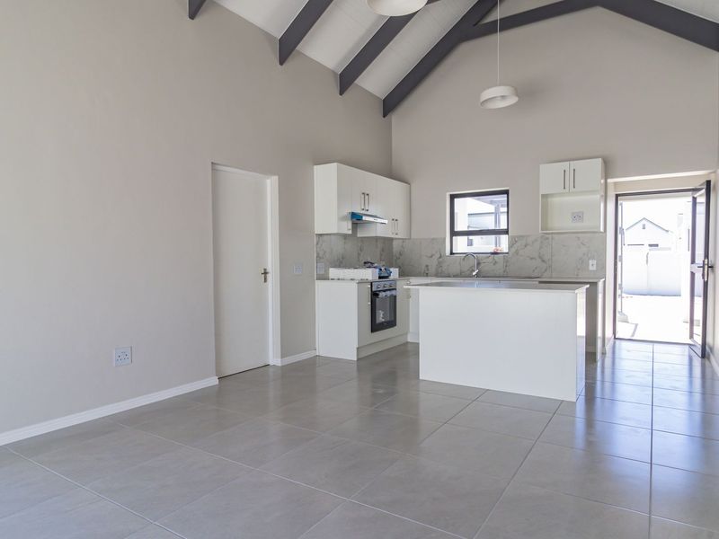 Bright open-plan living and kitchen area featuring vaulted ceilings with exposed rafters, modern tiled flooring, and a clean, contemporary kitchen layout.