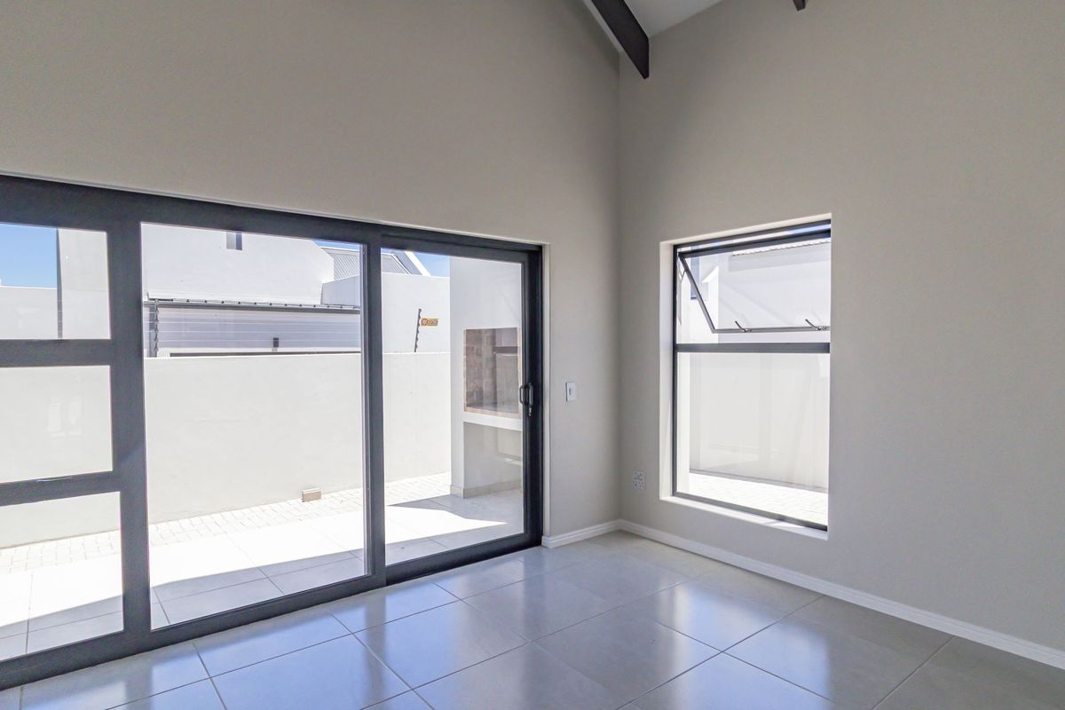 Bright and spacious living area featuring high vaulted ceilings, large sliding glass doors leading to an outdoor patio, and modern tiled flooring.