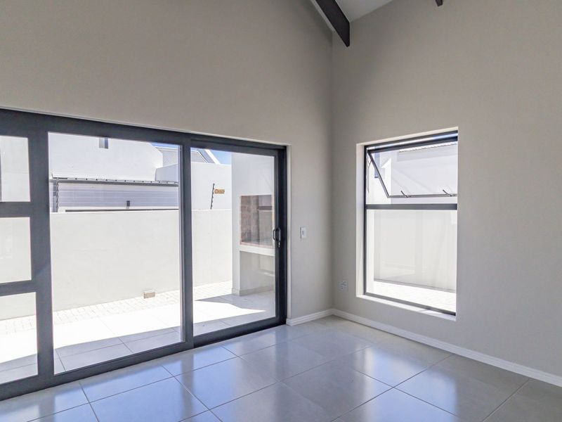 Bright and spacious living area featuring high vaulted ceilings, large sliding glass doors leading to an outdoor patio, and modern tiled flooring.