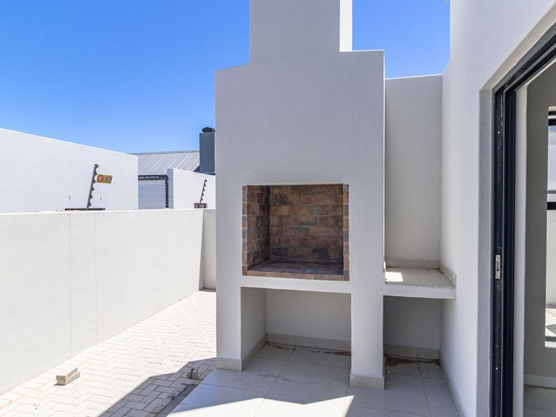 Outdoor patio area featuring a built-in brick braai, tiled flooring, and direct access to the interior via a sliding door.