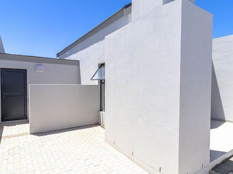 A clean, modern rear courtyard featuring paved flooring, a neutral exterior finish, and a secure external door.