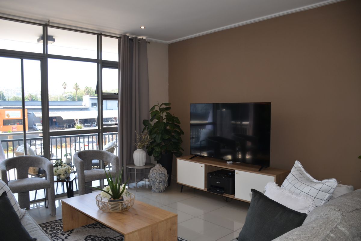A bright living room featuring large floor-to-ceiling windows, sliding glass doors, and neutral tiled flooring, offering a comfortable and well-lit space.
