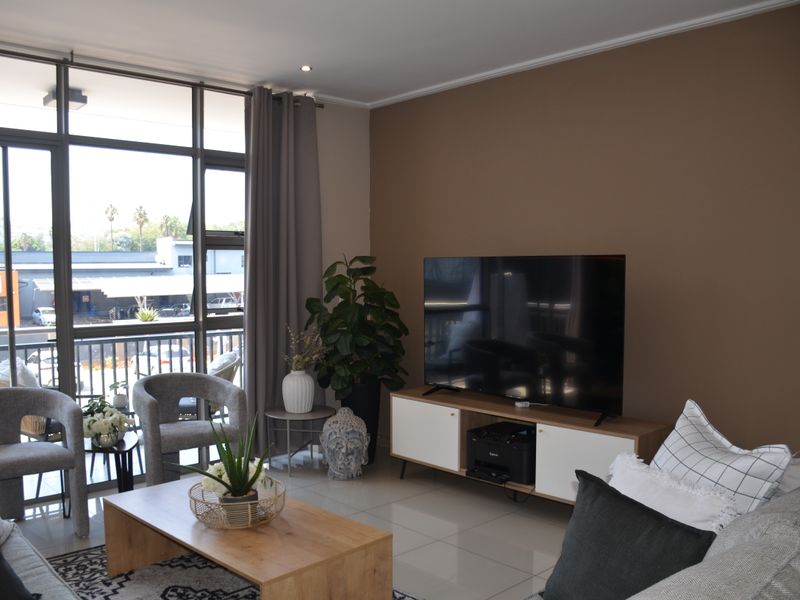 A bright living room featuring large floor-to-ceiling windows, sliding glass doors, and neutral tiled flooring, offering a comfortable and well-lit space.
