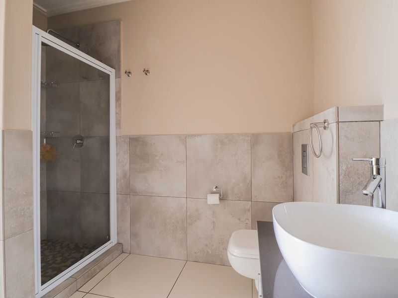 Modern bathroom featuring a glass-enclosed shower, wall-mounted toilet, and a contemporary vessel sink set on a sleek vanity countertop with neutral tiling.