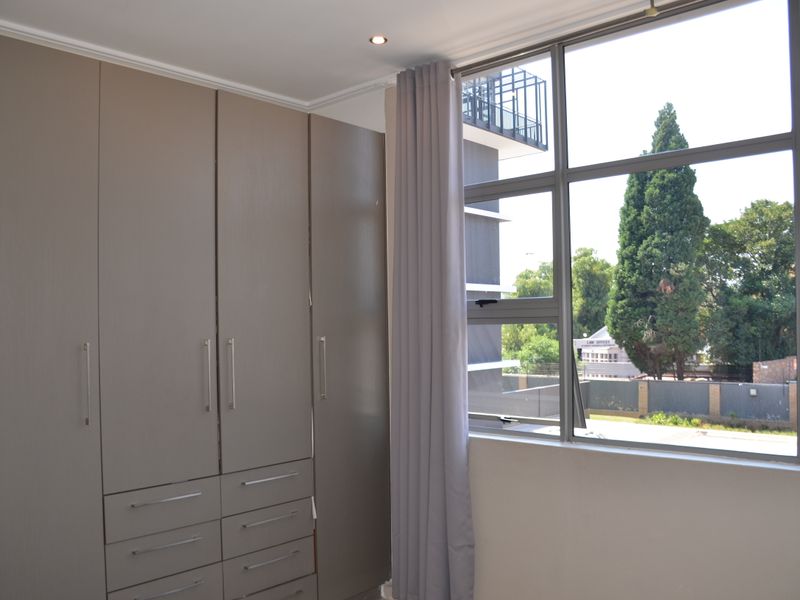 A bright bedroom featuring ample built-in cupboard storage, large aluminium-framed windows, and modern recessed downlighting.