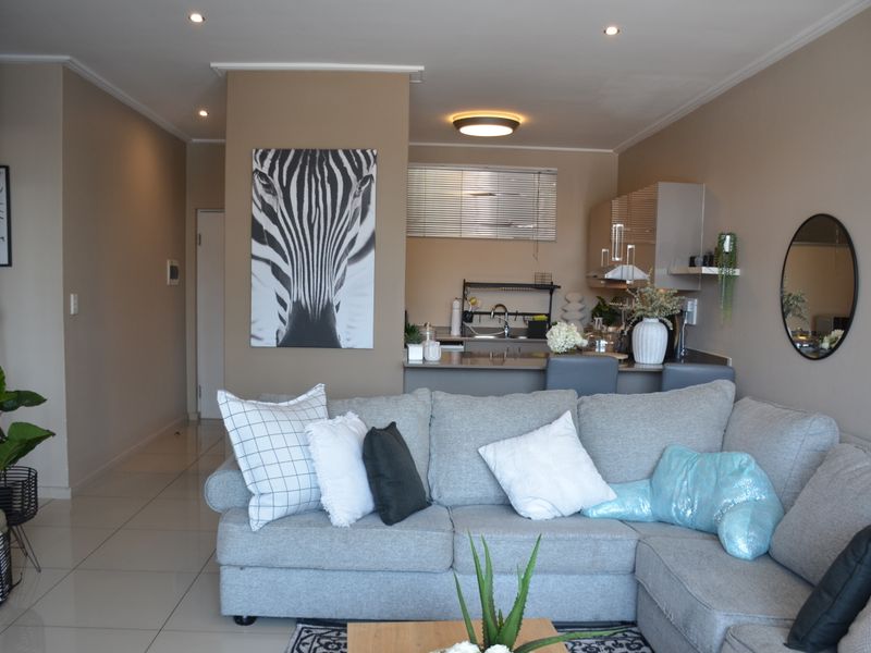An open-plan living area featuring a modern kitchen with breakfast bar, tiled flooring, and recessed lighting, creating a functional and cohesive living space.