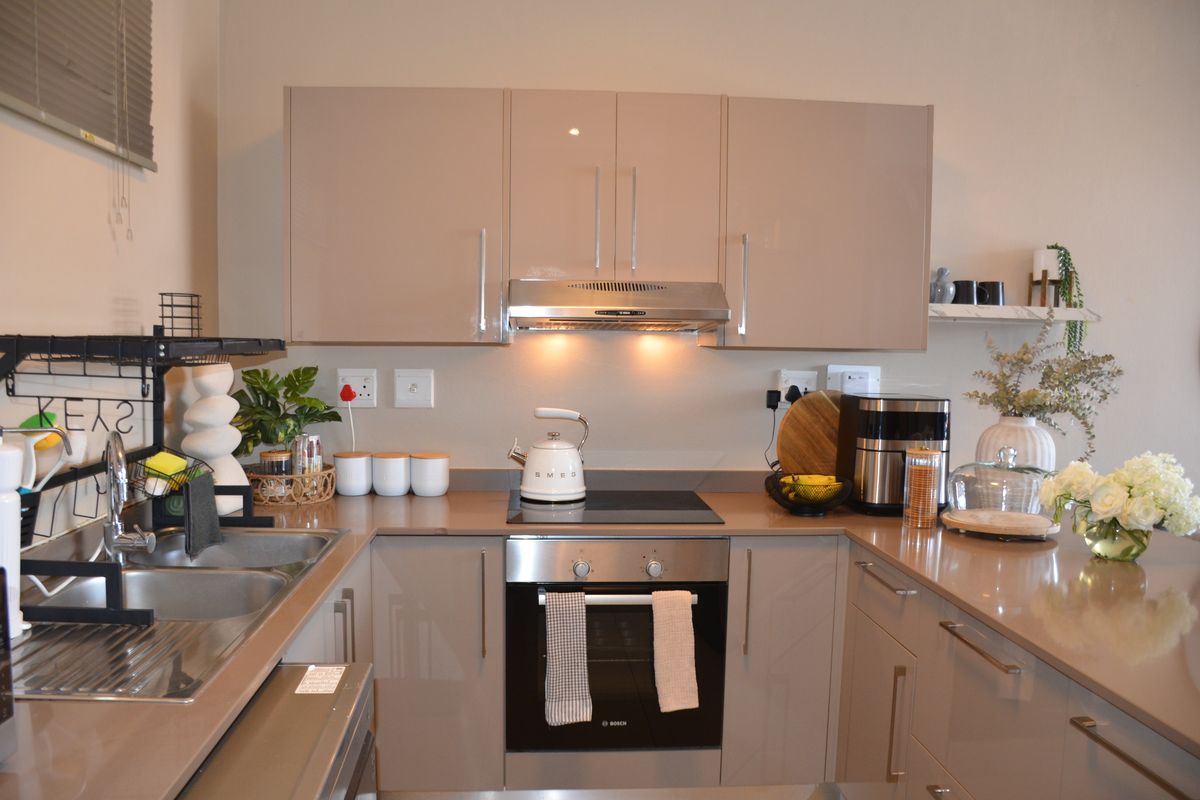A modern, well-maintained kitchen featuring sleek high-gloss cabinetry, stone countertops, integrated stainless steel appliances, and a functional layout.