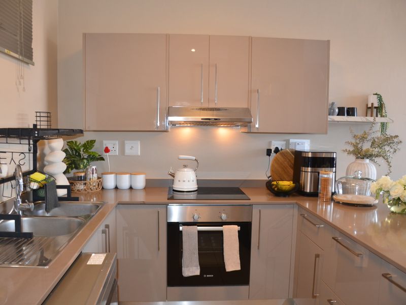A modern, well-maintained kitchen featuring sleek high-gloss cabinetry, stone countertops, integrated stainless steel appliances, and a functional layout.
