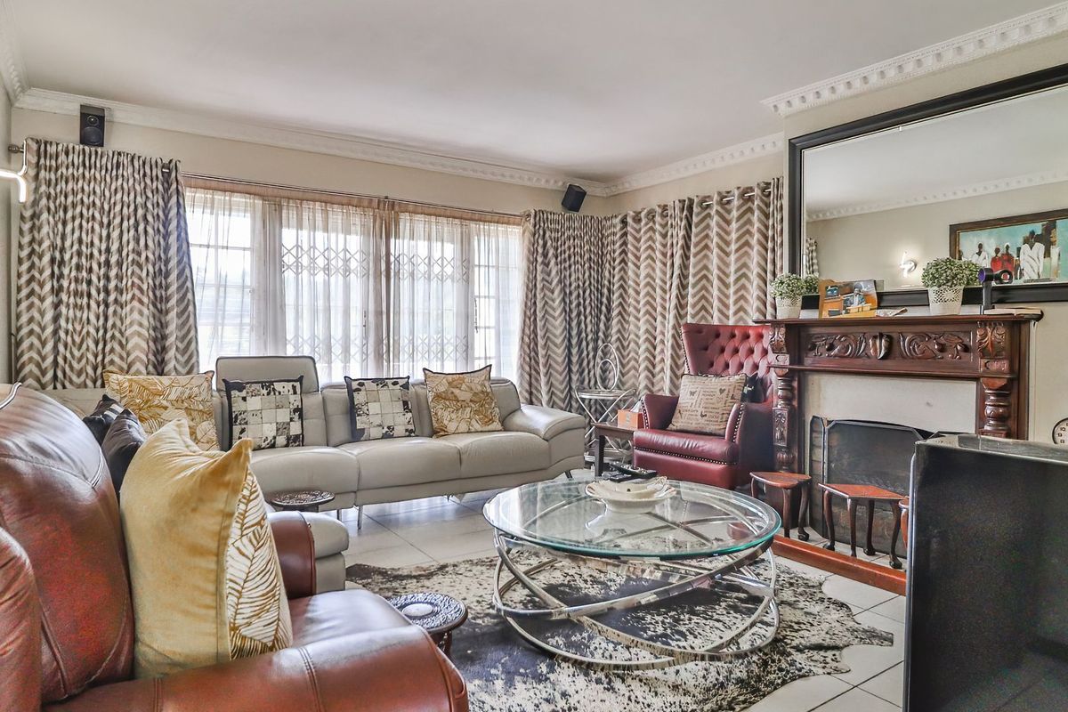 A comfortable living room featuring a traditional wooden fireplace mantel, tiled flooring, and large windows with security gates.