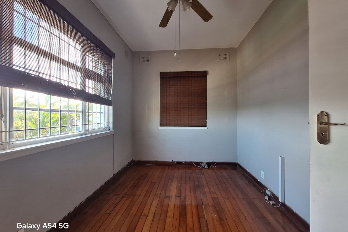 An empty bedroom featuring polished hardwood flooring, a ceiling fan, and windows fitted with security bars.