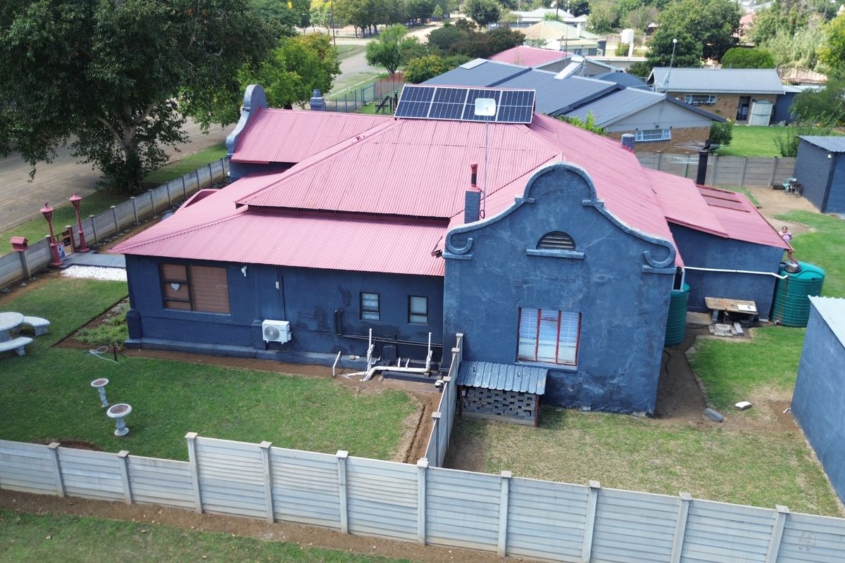 Aerial view of a residential property featuring a corrugated metal roof with solar panels, exterior wall finishes, and a surrounding precast concrete boundary wall.