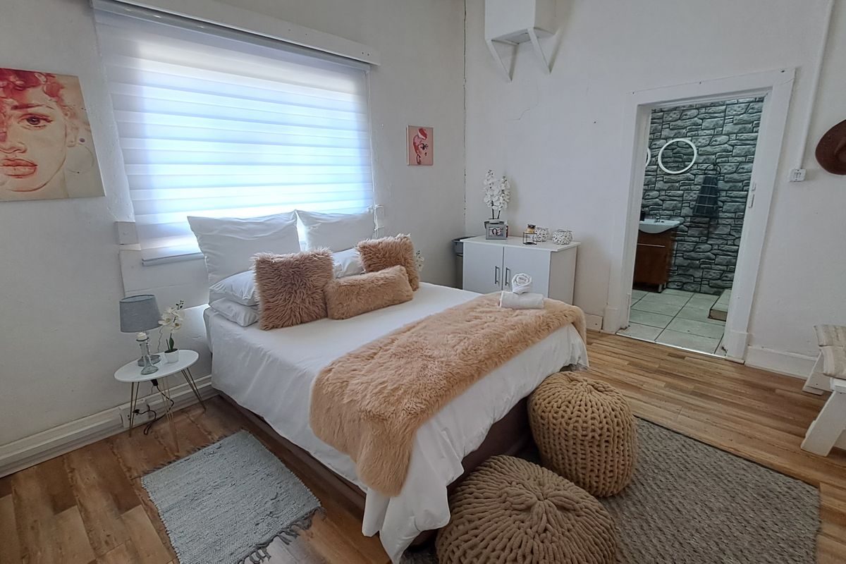 A bedroom featuring laminate flooring and roller blinds, with direct access to an en-suite bathroom with stone-cladding feature wall.