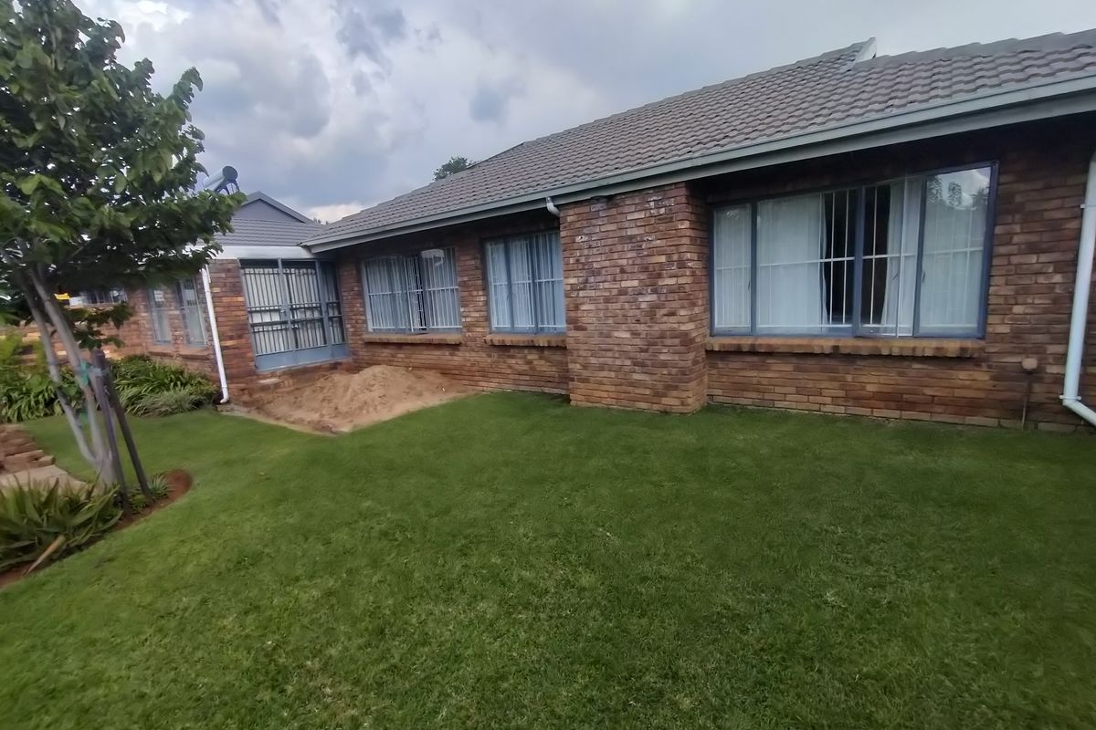 Rear view of a face brick duet property featuring a tiled roof, security bars on windows, and a well-maintained lawn.