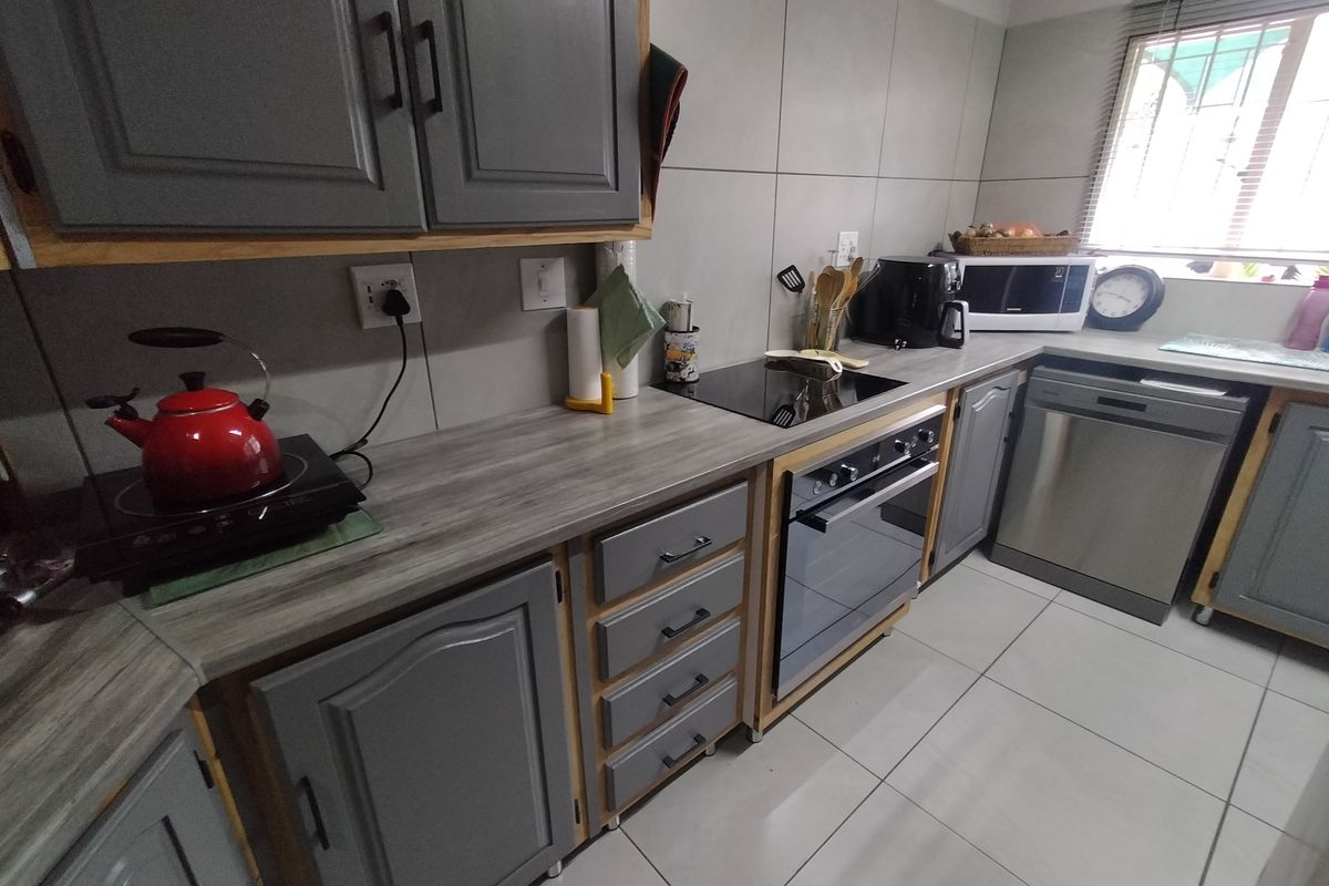 A functional kitchen featuring grey cabinetry, wood-look laminate countertops, tiled backsplash, and built-in oven with electric hob.