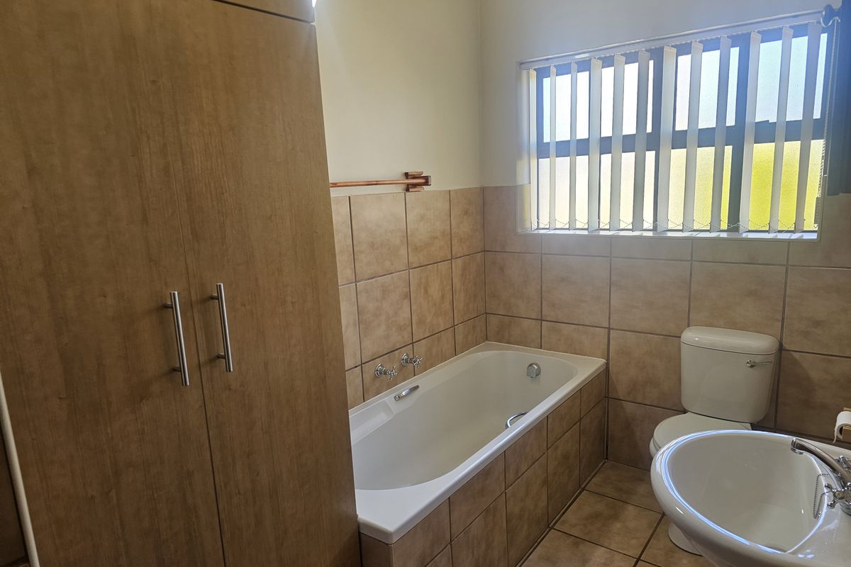 A functional bathroom featuring a built-in bathtub, pedestal basin, toilet, and floor-to-ceiling wooden cabinetry for storage.