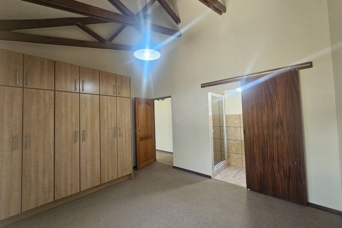 Spacious bedroom featuring high vaulted ceilings with exposed timber trusses, extensive built-in wooden cabinetry, and an en-suite bathroom accessed via a sliding door.
