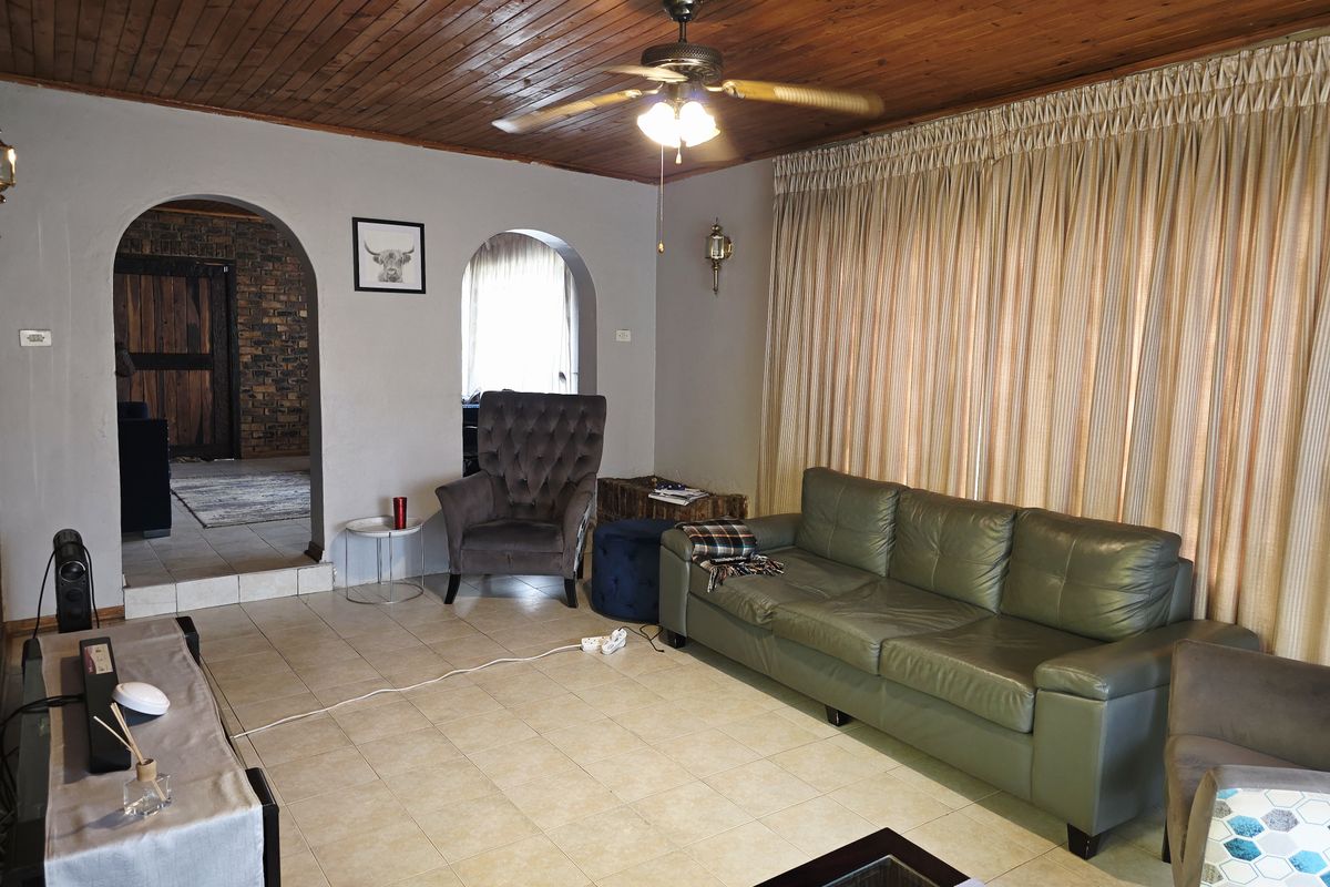 A living room featuring a timber-clad ceiling, ceiling fan, and arched doorways leading to adjacent spaces, finished with neutral floor tiles.