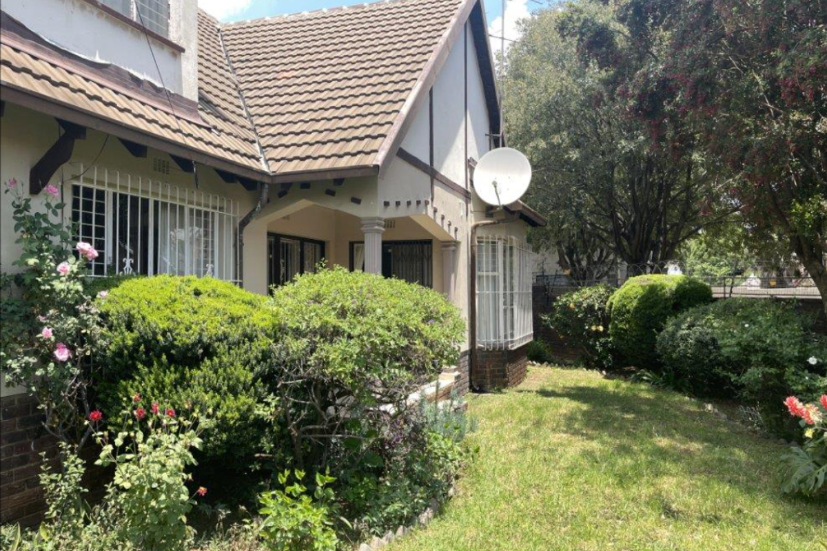 A view of the rear exterior of the house featuring a tiled roof, security bars on windows, and a small covered patio area.