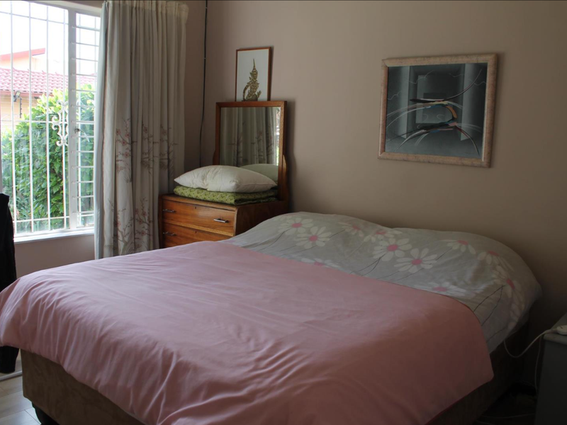 A standard bedroom featuring laminate flooring and a window fitted with security bars.