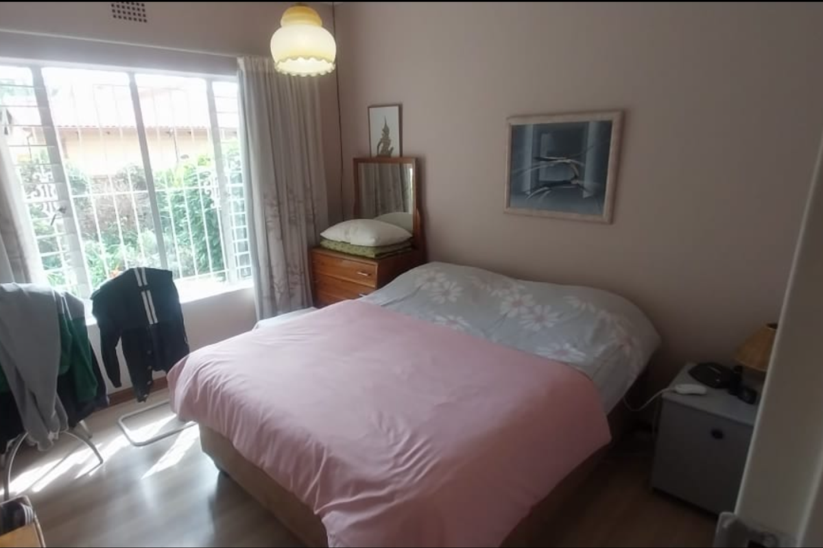 A standard bedroom featuring laminate flooring, a large window with security bars, and a central ceiling light fixture.