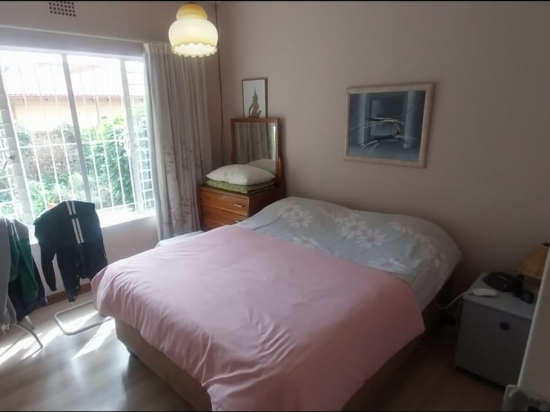 A standard bedroom featuring laminate flooring, a large window with security bars, and a central ceiling light fixture.