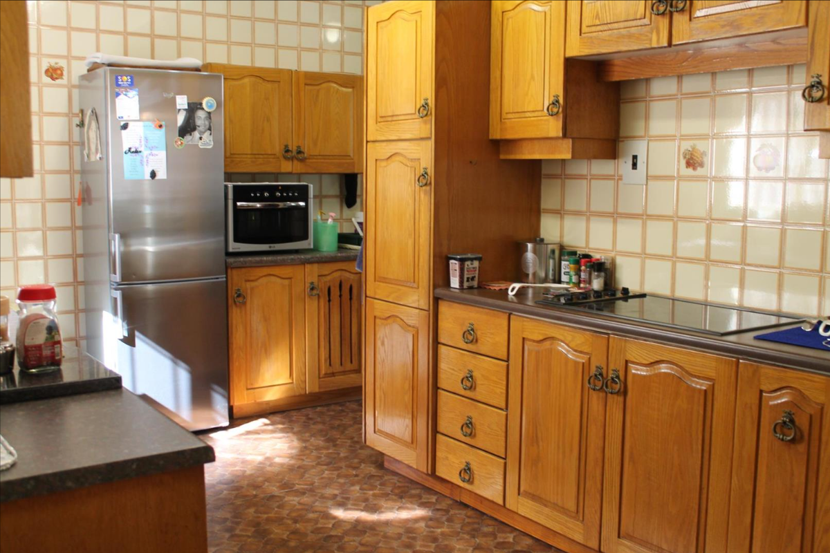 A traditional kitchen featuring wooden cabinetry, laminate countertops, a built-in oven, and an electric hob with tiled backsplash.